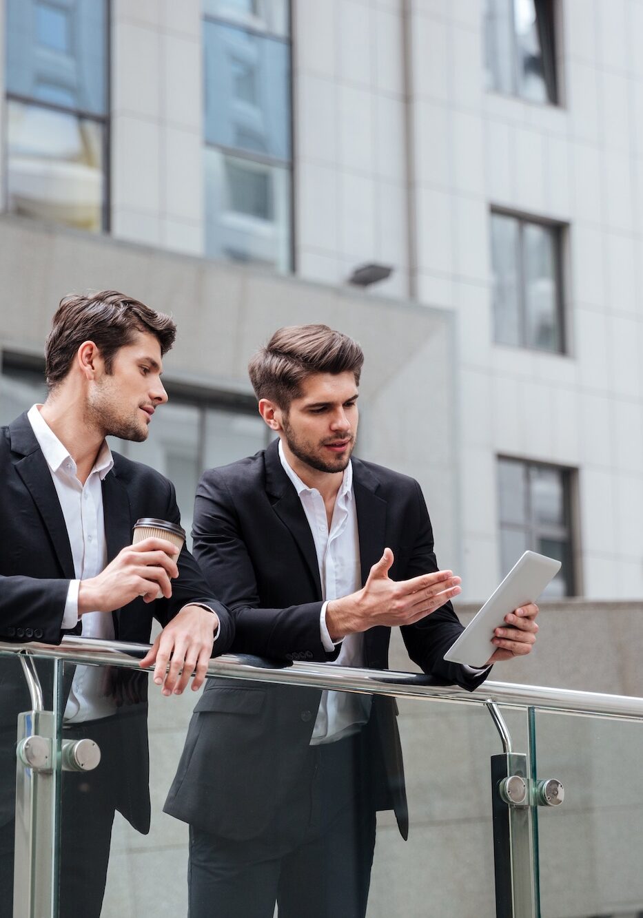 Two handsome young businessmen talking and using tablet in the city